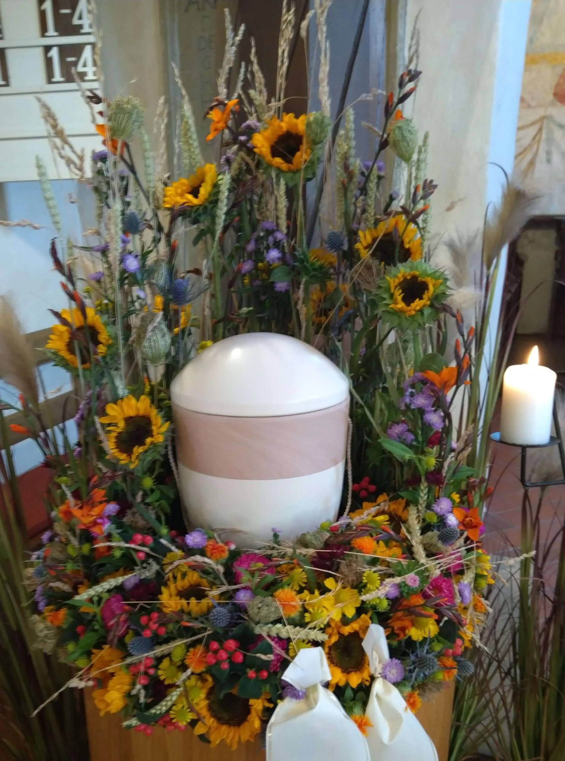 Urne mit Blumengesteck und Kerze auf einem Podest